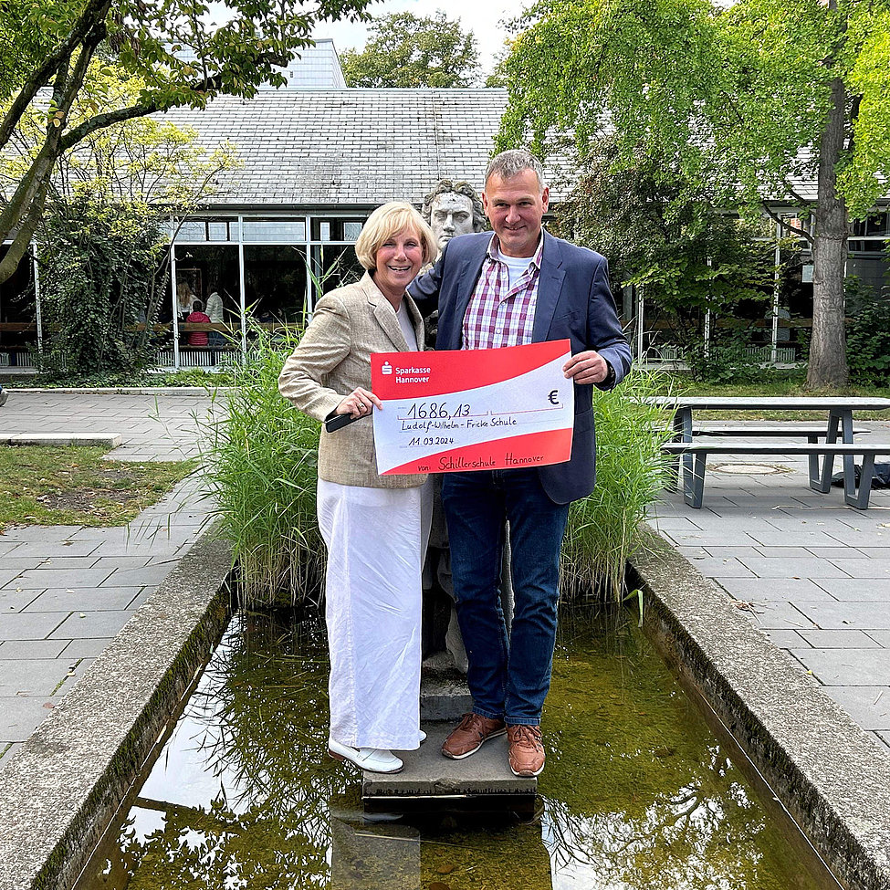 Scheckübergabe vor Schillerdenkmal zwei Personen halten großen Scheck über 1.686,13 Euro